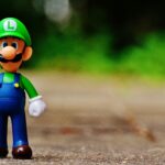 Close-up of a Luigi figurine from a videogame standing on outdoor pavement, showcasing fun and play.