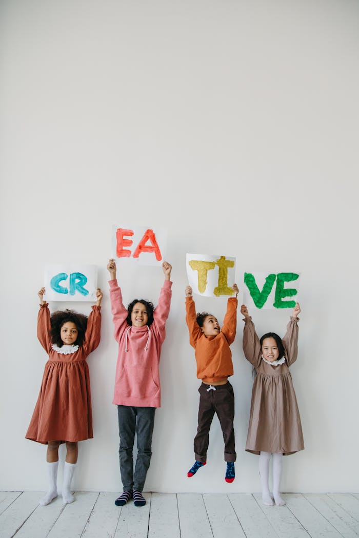 Group of children holding up colorful letters spelling 'CREATIVE' indoors.