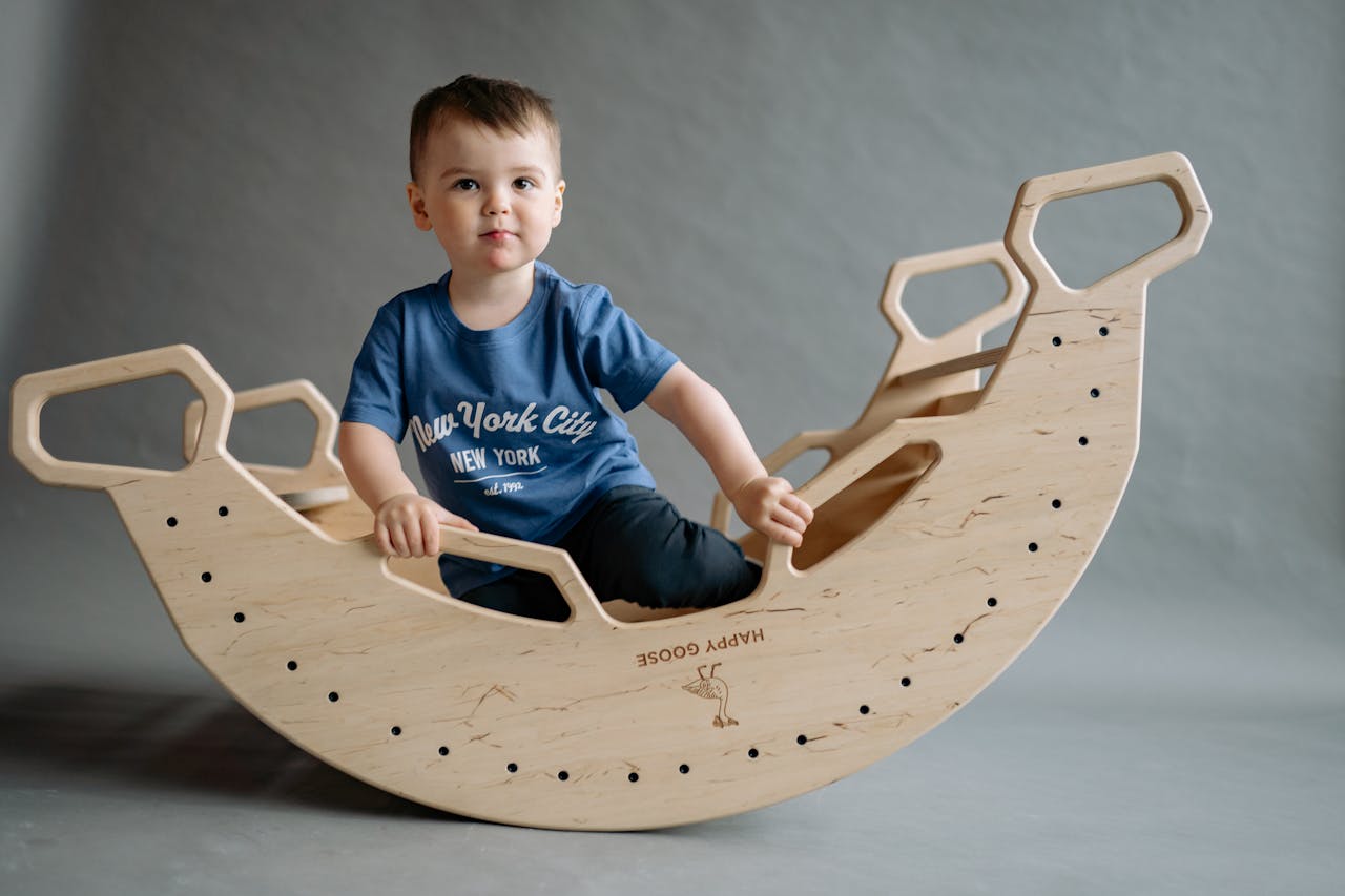 Cute child in a blue t-shirt sits on a wooden rocker in a studio setting.